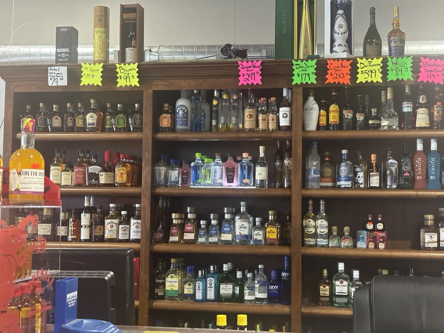 Wooden shelves behind the counter displaying whiskey, tequila, vodka, liqueurs and featured bottles